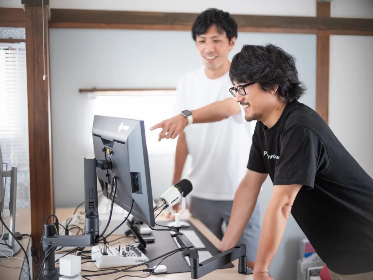 同じ画面を見ながら笑顔で作業するメガネの人物