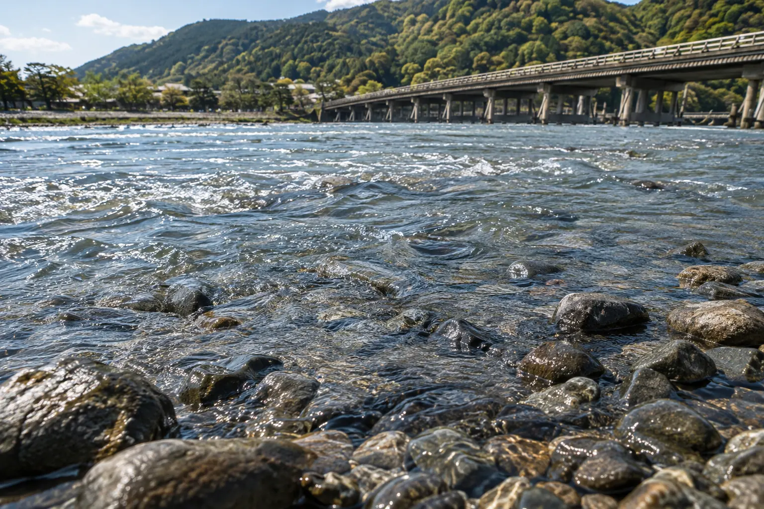 桂川の岸辺の石を洗う流れと、その奥に見える渡月橋