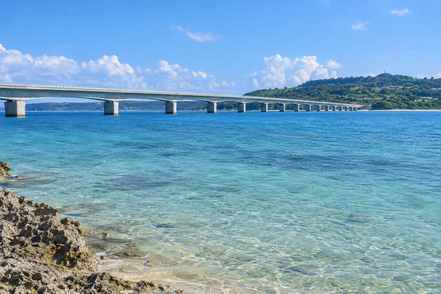 海辺から横方向に眺める古宇利大橋と、その先の古宇利島の緑
